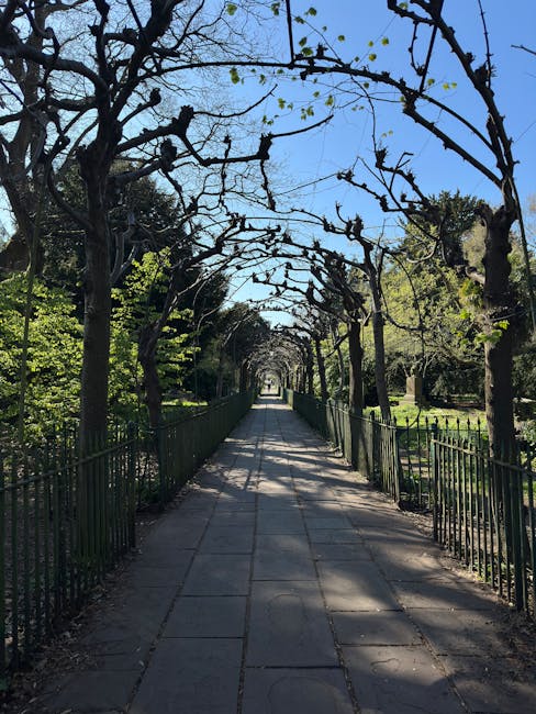 A two-story brick house with a rounded bay window on the upper floor and a smaller bay window on the ground floor, situated at the end of a paved stone pathway. The pathway is flanked by lush, well-ma